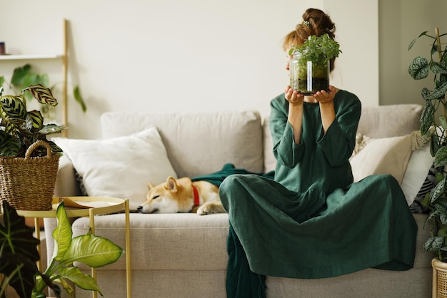 Mujer joven sentada en el sofá en casa con un florario DIY en un frasco de vidrio