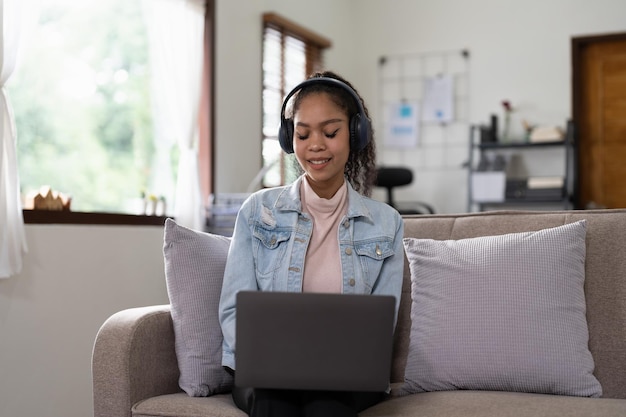 Mujer joven sentada en un sofá en casa videollamada chateando con amigos usando una computadora portátil en casa