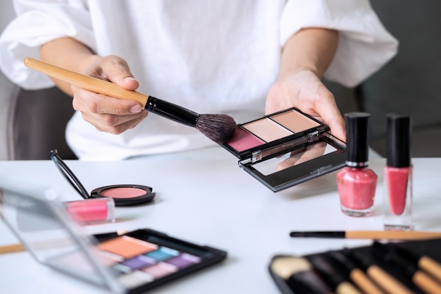 Mujer joven sentada en el sofá y haciendo maquillaje en casa