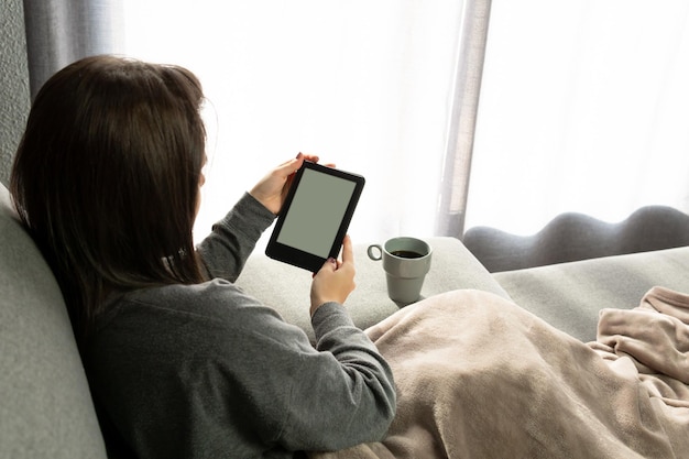 Mujer joven sentada en el sofá leyendo con su ebook