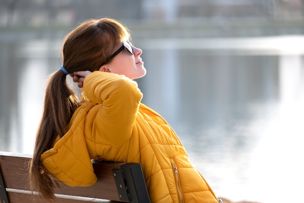 Mujer joven sentada sola en un banco del parque relajante en un cálido día de otoño.