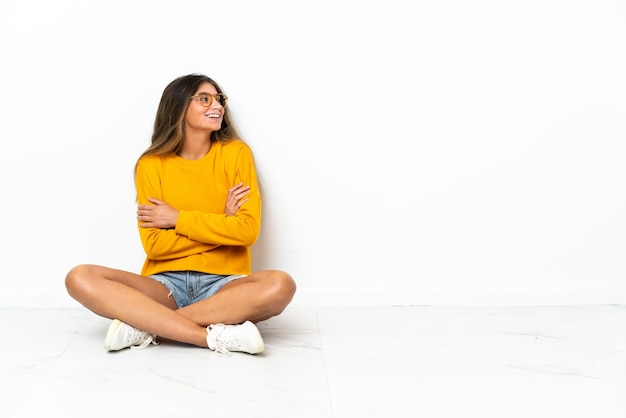 Foto mujer joven sentada en el suelo aislado en la pared blanca feliz y sonriente