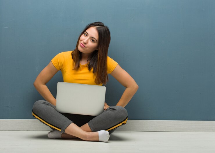 Foto mujer joven sentada en el suelo con una computadora portátil regañando a alguien muy enojada