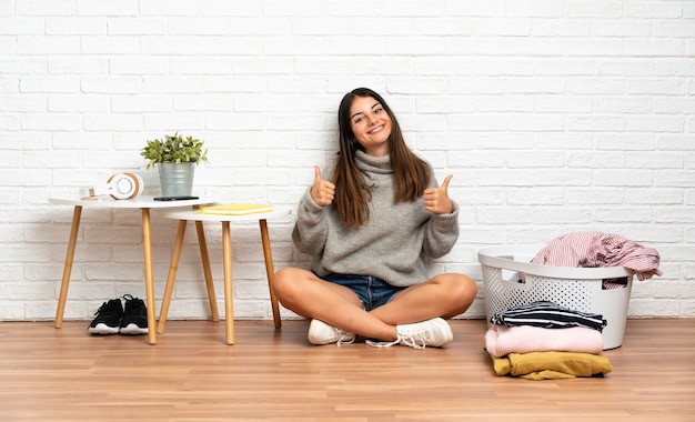 Mujer joven sentada en el suelo en el interior con canasta de ropa orgulloso y satisfecho de sí mismo