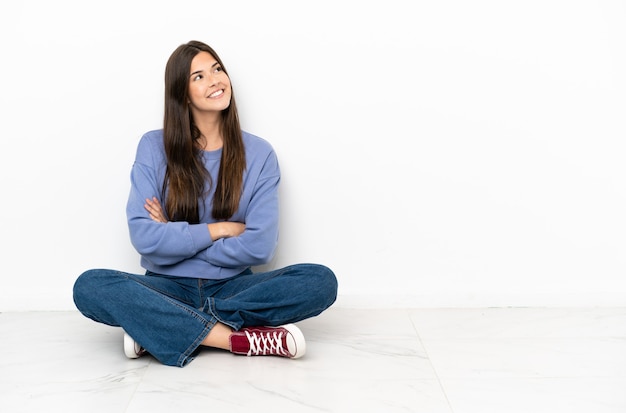 Foto mujer joven sentada en el suelo mirando hacia arriba mientras sonríe
