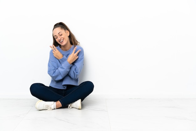 Mujer joven sentada en el suelo sonriendo y mostrando el signo de la victoria