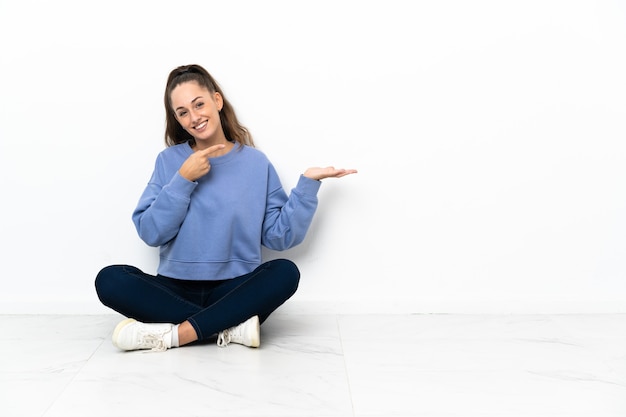 Mujer joven sentada en el suelo sosteniendo copyspace imaginario en la palma para insertar un anuncio