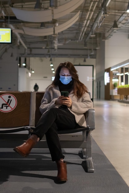 Foto una mujer joven está sentada en el vestíbulo del aeropuerto mirando su teléfono.