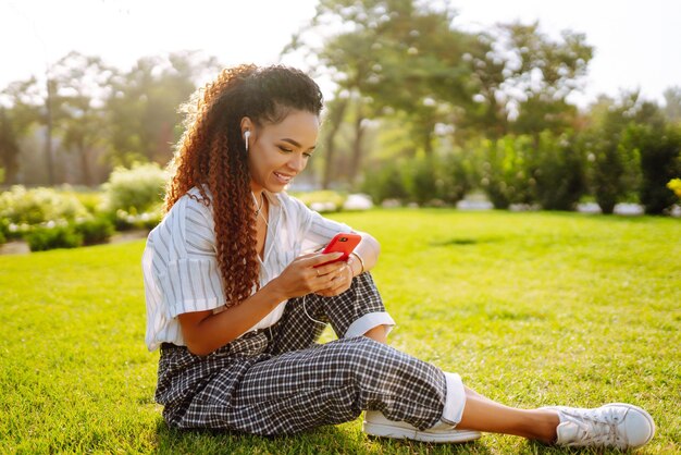 mujer joven, sentado, en, pasto verde, en el parque, con, teléfono, bastante, mujer, escuchar música