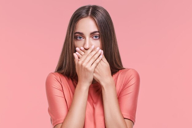 Mujer joven seria que cubre la boca con ambas manos guardando un secreto