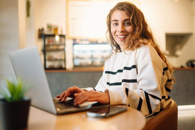 Mujer joven se sienta en un café y trabaja en la computadora Concepto de educación independiente de blogs de negocios
