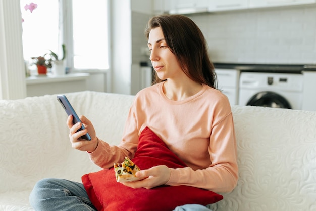 Una mujer joven se sienta cómodamente en su sofá navegando su teléfono inteligente con una expresión de contenido en su