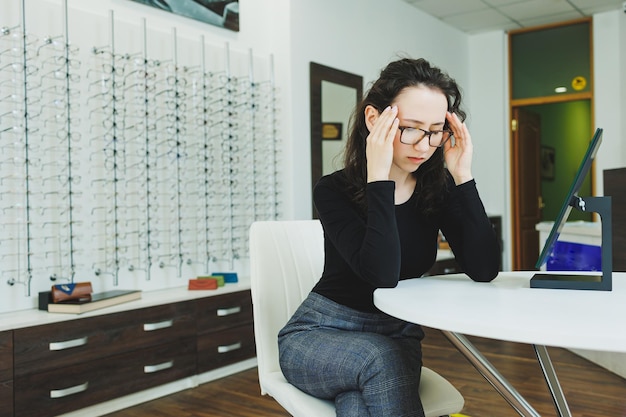 Una mujer joven se sienta y elige gafas en un salón de oftalmología Mala vista