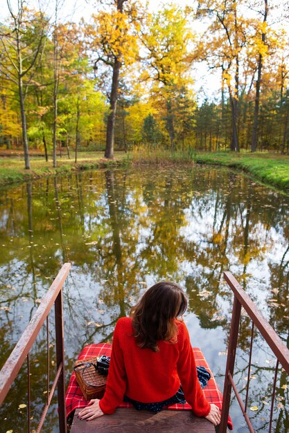 Foto una mujer joven se sienta con la espalda en un puente cerca de un lago en un día soleado hermoso otoño