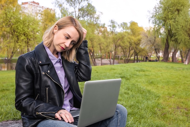 Una mujer joven se sienta en un parque y trabaja con un concepto de estilo de vida de educación empresarial portátil