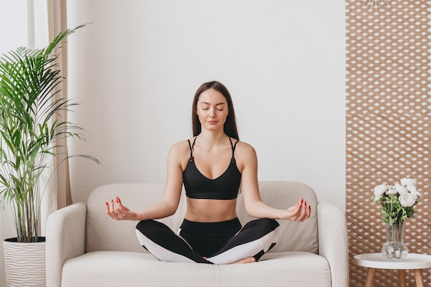 Una mujer joven se sienta en una posición de loto y medita Clases de yoga en casa