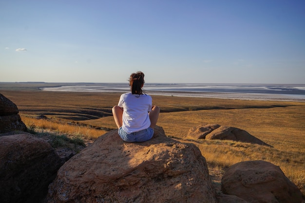 Una mujer joven se sienta en el suelo al atardecer y mira a lo lejos el