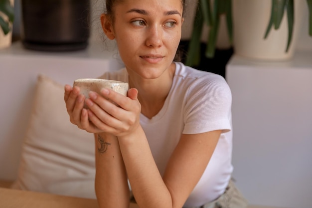 Una mujer joven se sienta con una taza hecha a mano de arcilla para disfrutar y relajarse