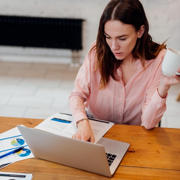 Mujer joven se sienta con una taza en su computadora portátil durante un descanso de trabajo