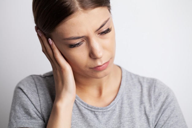 Una mujer joven siente dolor de cabeza y sostiene el lugar del dolor con las manos.