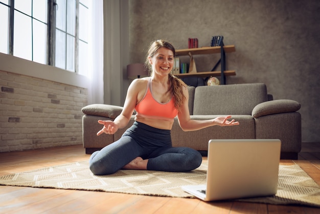 Mujer joven sigue con una computadora portátil un ejercicio de gimnasio. Está en casa por cuarentena por coronavirus codiv-19