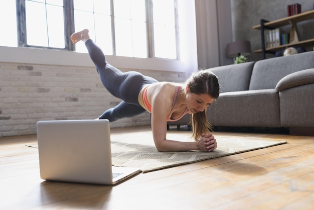 Mujer joven sigue con una computadora portátil un ejercicio de gimnasio.