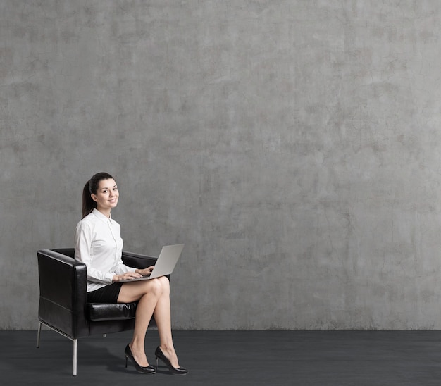 mujer joven, en, sillón de cuero, cerca, pared concreta