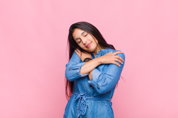 Mujer joven sintiéndose enamorada, sonriendo, abrazándose y abrazándose a sí misma, permaneciendo soltera, siendo egoísta y egocéntrica