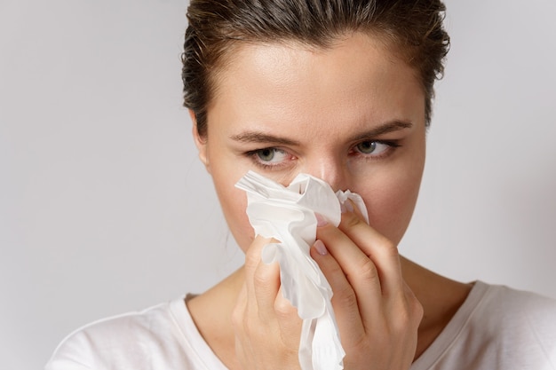 Mujer joven con un síntoma de secreción nasal está soplando en el pañuelo de papel