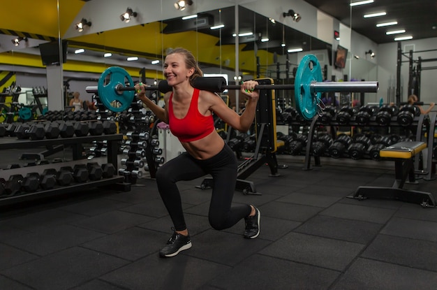 Mujer joven slim fit practicando estocadas con una barra sobre sus hombros en un gimnasio moderno