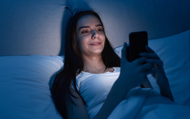 Mujer joven con smartphone en la cama por la noche