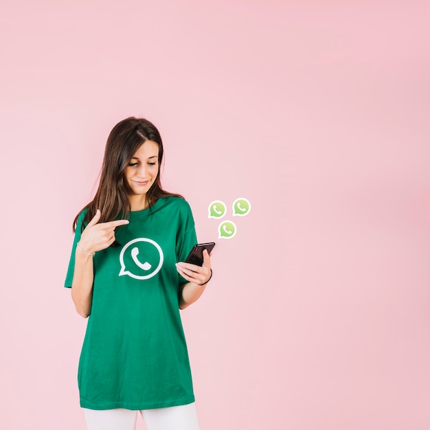 Mujer joven con smartphone cerca de icono de WhatsApp