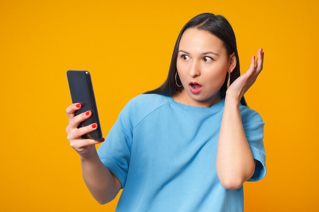 Mujer joven con smartphone y sonriendo. Sobre un fondo amarillo.