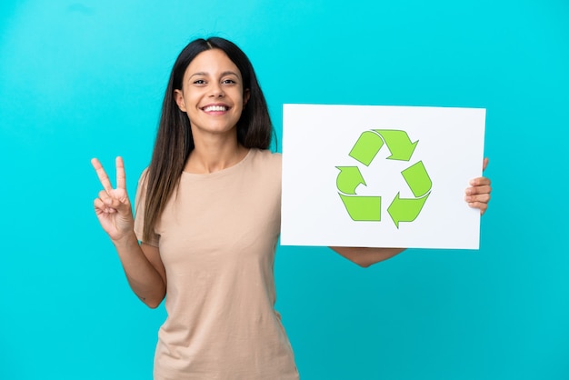 Mujer joven sobre antecedentes aislados sosteniendo un cartel con el icono de reciclaje y celebrando una victoria