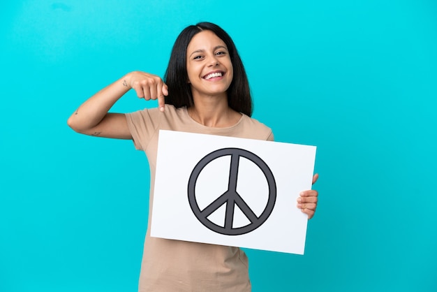 Foto mujer joven sobre antecedentes aislados sosteniendo un cartel con el símbolo de la paz y apuntando