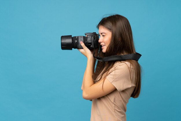 Mujer joven sobre azul aislado con una cámara profesional