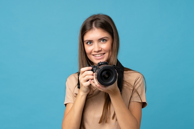 Mujer joven sobre azul aislado con una cámara profesional