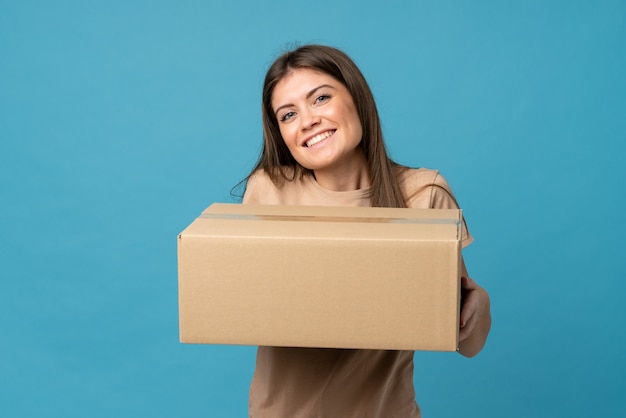 Mujer joven sobre azul aislado sosteniendo una caja para moverlo a otro sitio