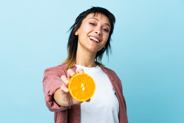 Mujer joven sobre azul aislado sosteniendo una naranja