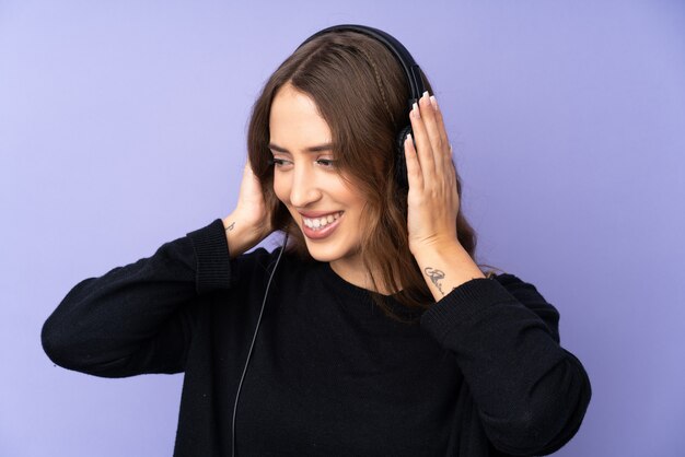 Mujer joven sobre escuchar música de pared púrpura aislado