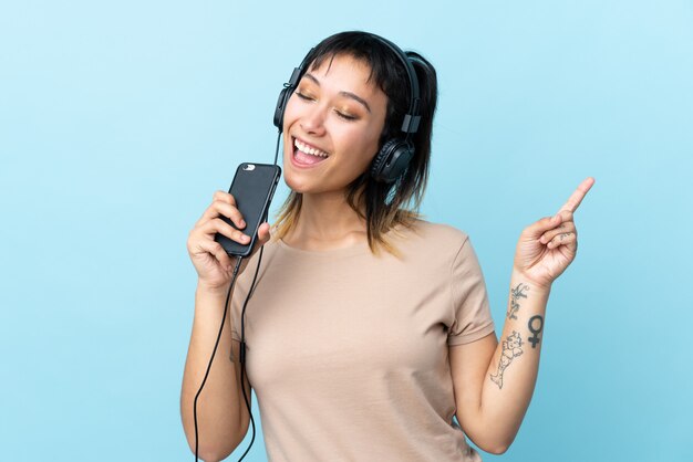 Mujer joven sobre espacio azul aislado escuchando música con un móvil y cantando