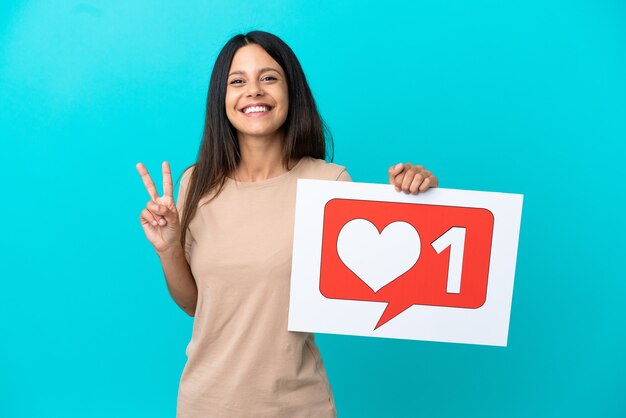 Mujer joven sobre fondo aislado sosteniendo una pancarta con el icono Me gusta y celebrando una victoria