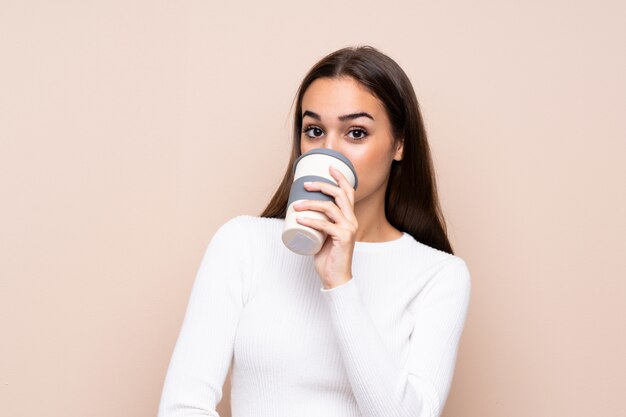 Mujer joven sobre fondo aislado sosteniendo y tomando un café para llevar