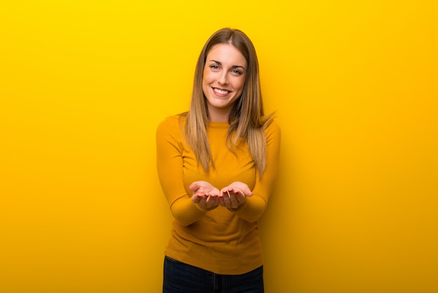 Mujer joven sobre fondo amarillo sosteniendo copyspace imaginario en la palma para insertar un anuncio