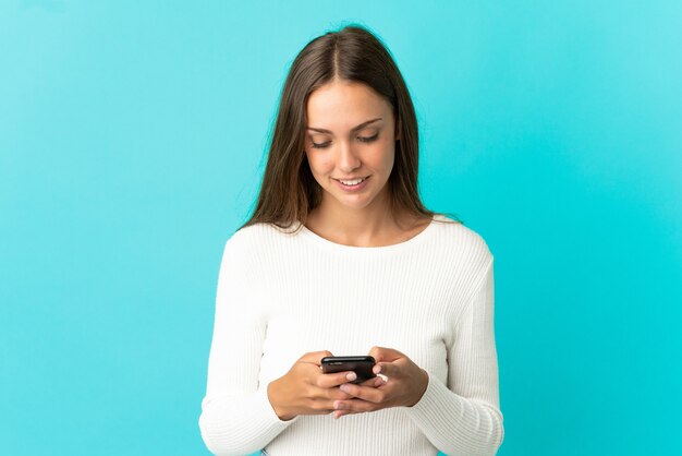 Mujer joven sobre fondo azul aislado enviando un mensaje con el móvil