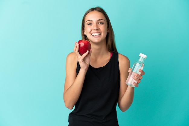 Mujer joven sobre fondo azul aislado con una manzana y con una botella de agua