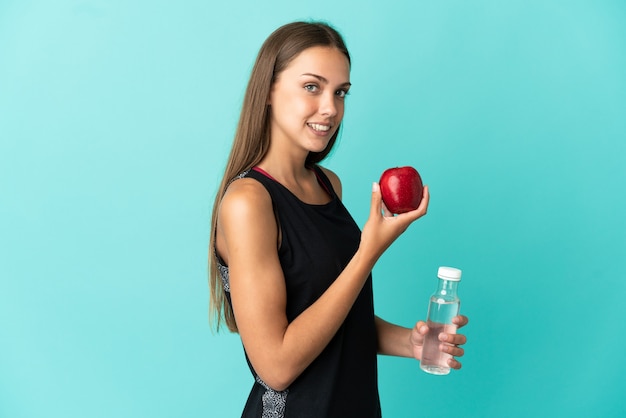 Mujer joven sobre fondo azul aislado con una manzana y con una botella de agua