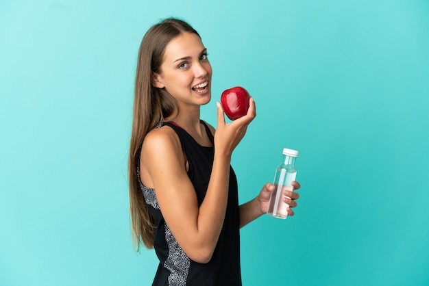 Mujer joven sobre fondo azul aislado con una manzana y con una botella de agua