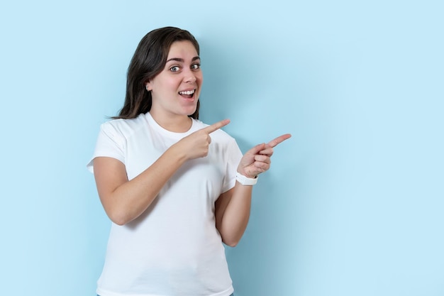 Mujer joven sobre fondo azul aislado señalando con el dedo al lado