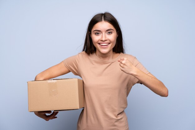 Mujer joven sobre fondo azul aislado sosteniendo una caja para moverlo a otro sitio